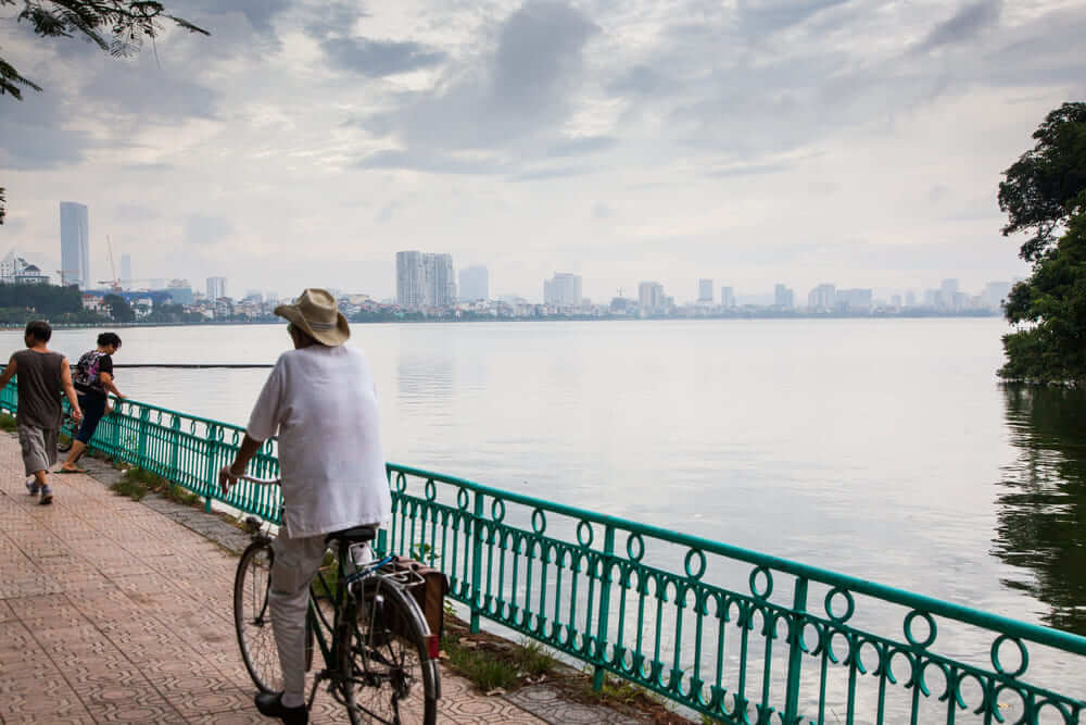 Elderly cyclist on West Lake path in peaceful Hanoi morning